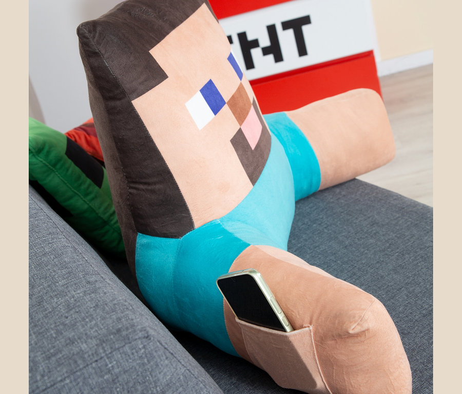Minecraft Relaxkissen Steve liegt auf einem grauen Sofa, ein Handy steckt in seiner Tasche.