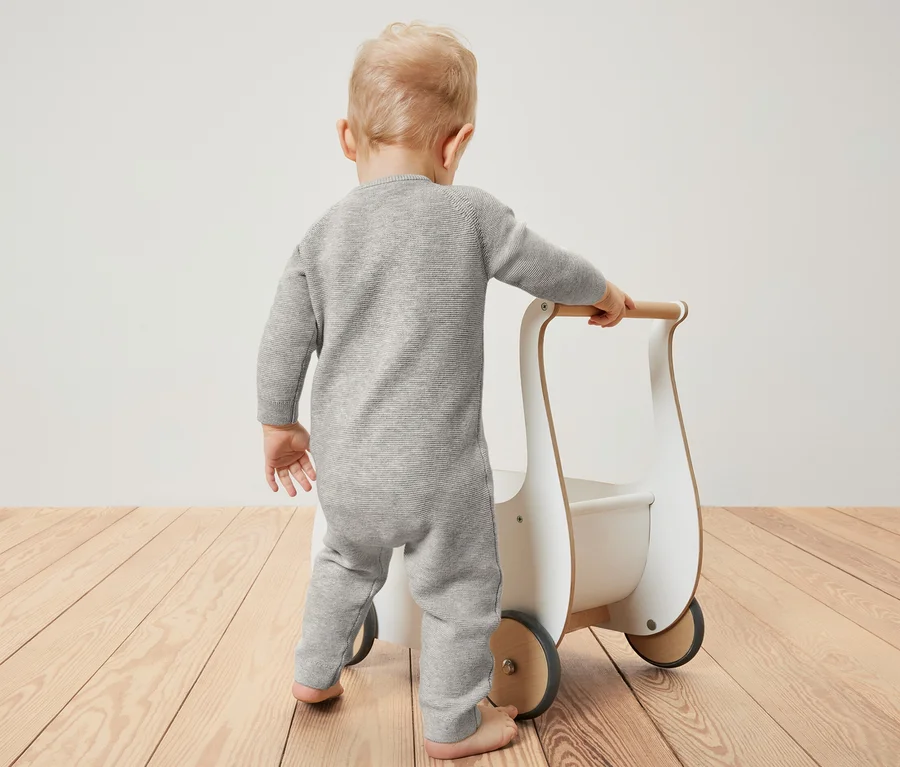 Baby im Strickoverall schiebt Lauflernwagen.