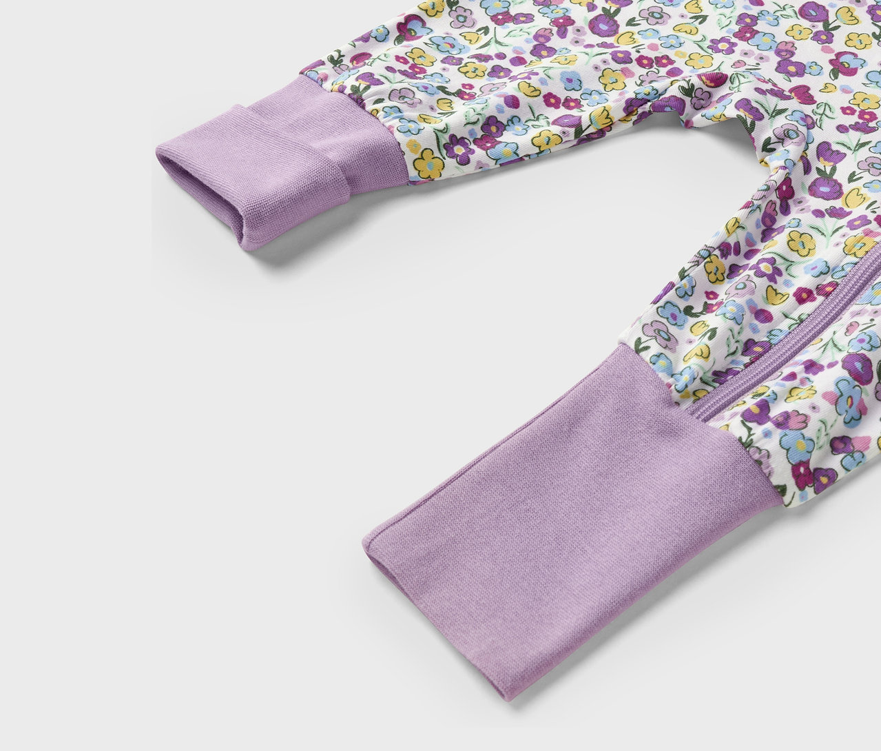Detailaufnahme eines lila Overalls mit Blumenmuster, Reißverschluss und langen Ärmeln.