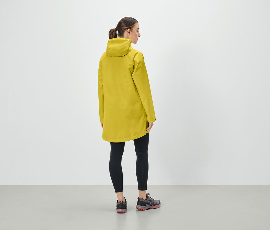 Frau in gelber Kapuzenjacke, schwarzen Leggings und Sportschuhen steht mit dem Rücken zur Kamera.