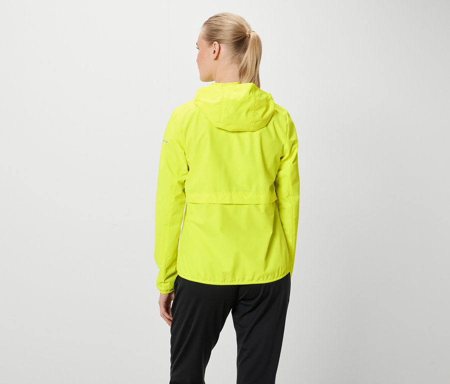 Von hinten ist eine Frau mit blonden, zu einem Pferdeschwanz zusammengebundenen Haaren zu sehen, die eine neongelbe Kapuzenjacke und eine schwarze Hose trägt.