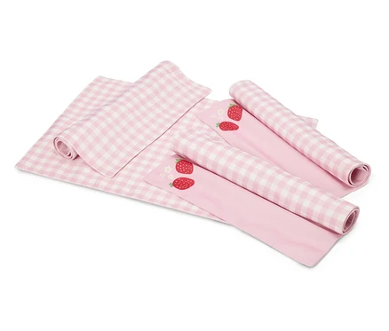 Auf einem weißen Hintergrund liegen eine rosa-weiß karierte Decke und zwei rosa Stoffe mit Erdbeermotiven, die teilweise aufgerollt sind.
