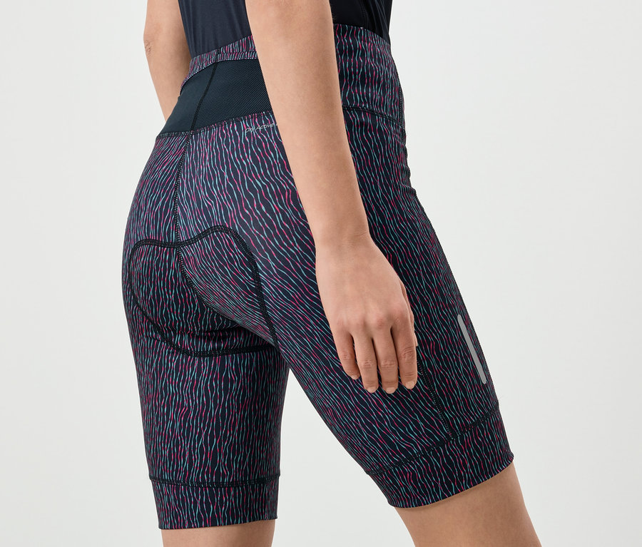 Nahaufnahme einer Frau, die gemusterte Radsportshorts mit einer schwarzen Taille und einer reflektierenden Lasche am Bein trägt.