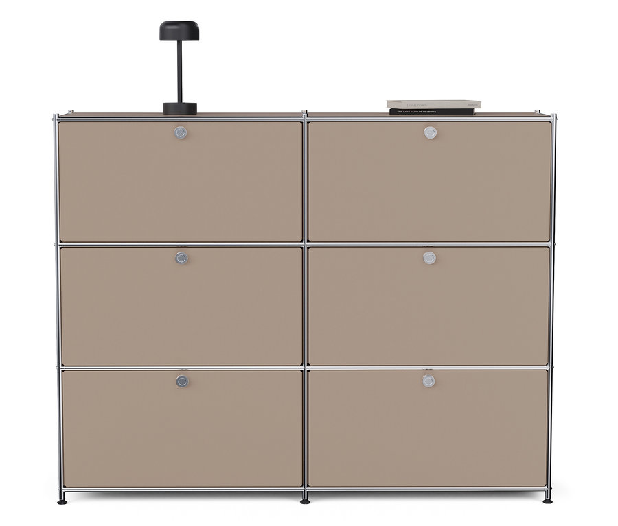Eine taupefarbene Metall-Kommode »CN3« mit sechs Klappfächern steht vor einem weißen Hintergrund. Auf der Kommode stehen eine Lampe und ein Buch.