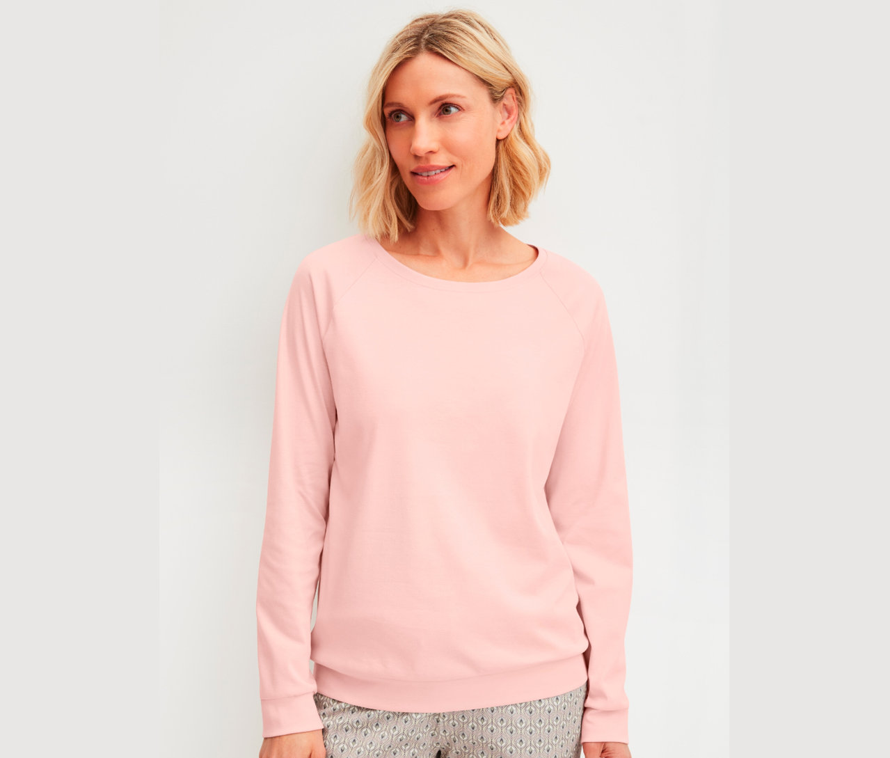 Frau mit blonden, schulterlangen Haaren, trägt ein langärmliges, rosa Oberteil.