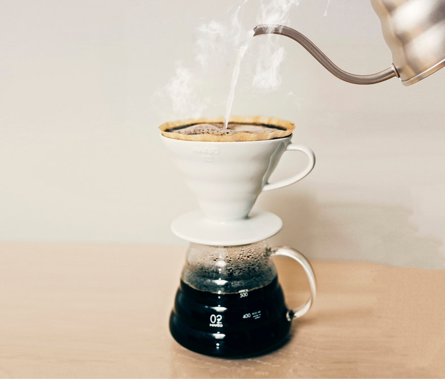 Heißes Wasser wird in einen HARIO V60 Keramikfilter gegossen, der auf einer Glaskaraffe steht.