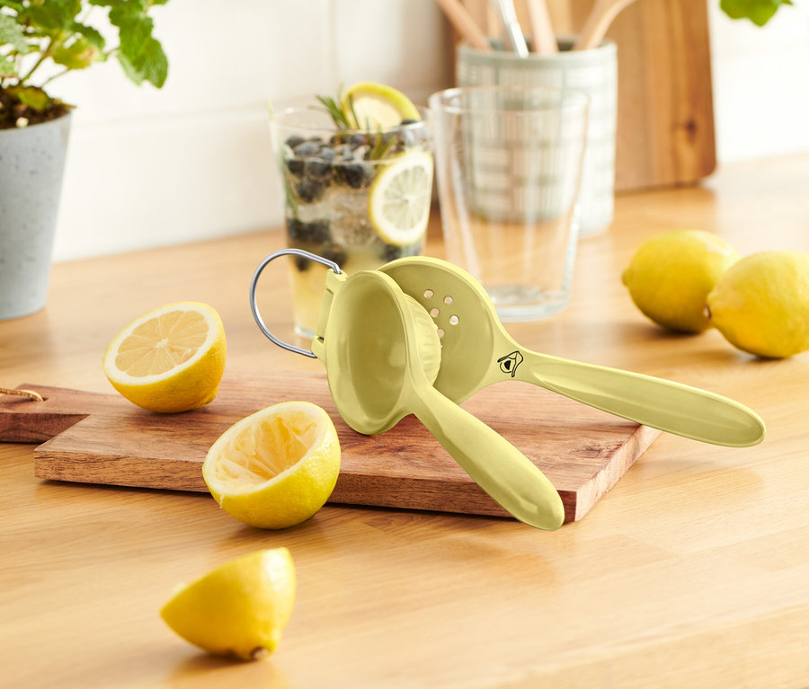 Auf einem Holztisch stehen ein paar Zitronen, ein Zitronenentsafter und ein Glas Limonade.