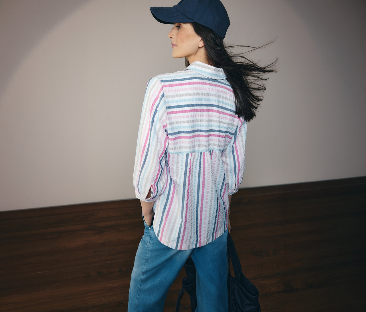 Frau mit Jeans und blau gestreifter CECIL Hemdbluse und Kappe, von hinten gesehen.