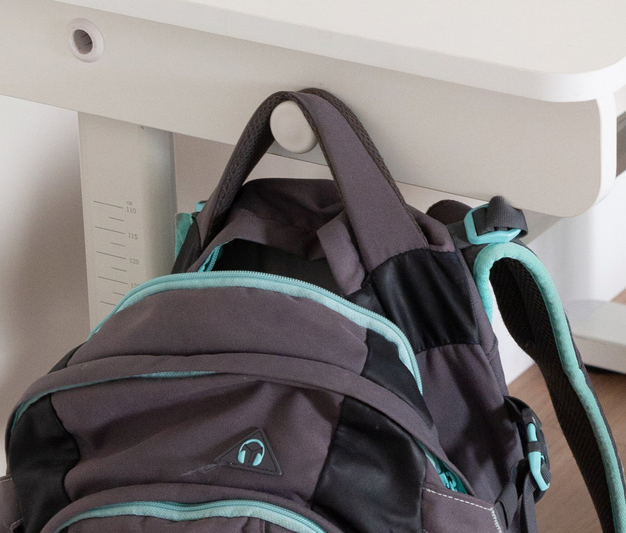 Grauer Rucksack mit türkisfarbenen Akzenten hängt an einem weißen Tisch.