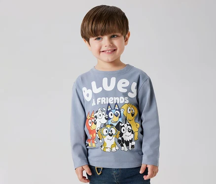 Lächelnder Junge trägt ein NAME IT Kinder-Langarmshirt »BLUEY« mit Bluey- und Freunde-Motiv.