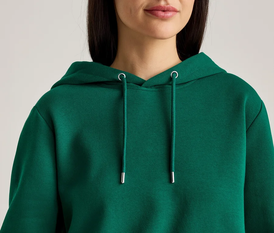 Nahaufnahme einer Frau mit dunkelbraunen Haaren, die einen grünen Kapuzenpullover mit Kordelzug trägt.