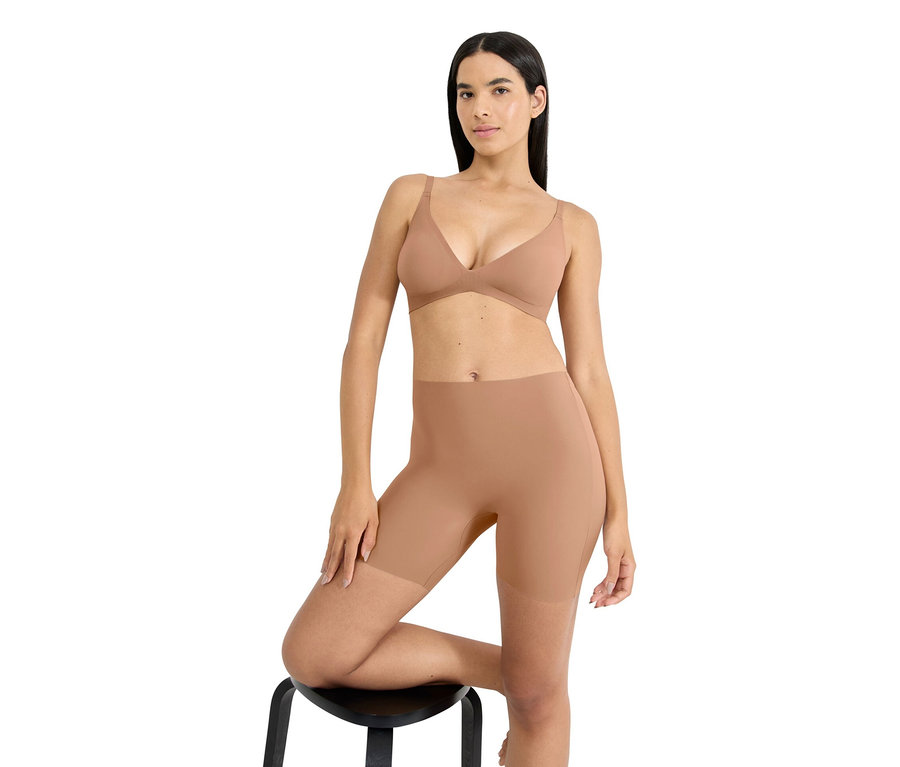 Frau posiert auf einem Hocker und trägt BH sowie Shapewear-Shorts in einem Hautton.