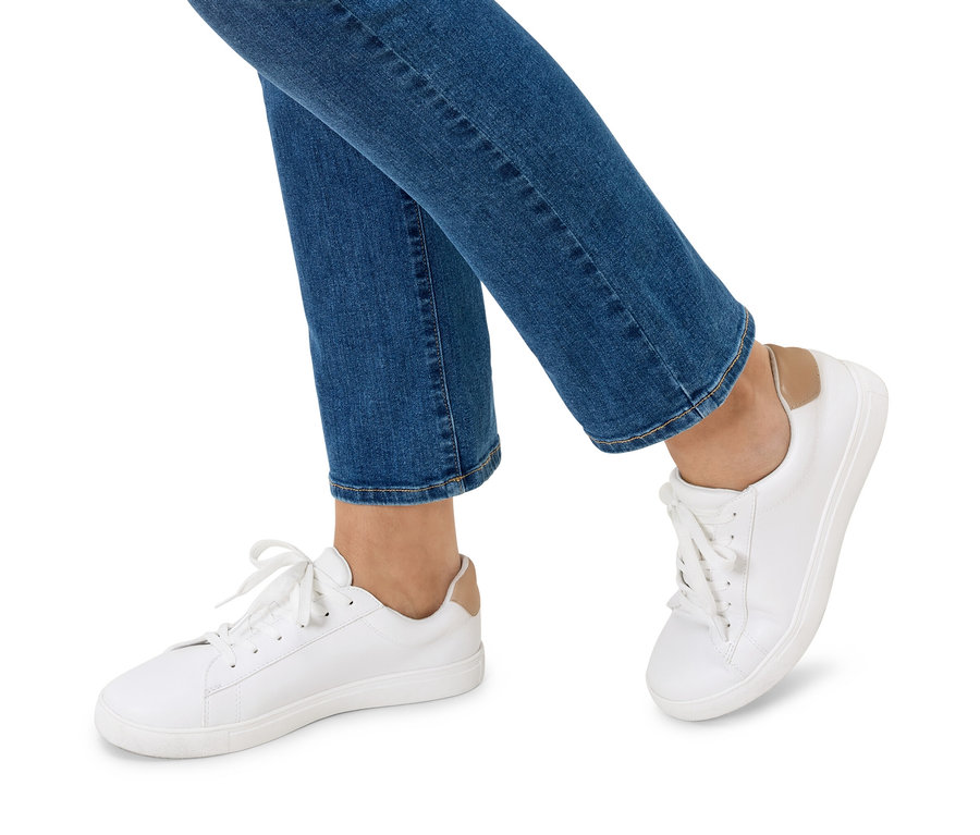 Beine einer Person in blauen Jeans und weißen Turnschuhen.