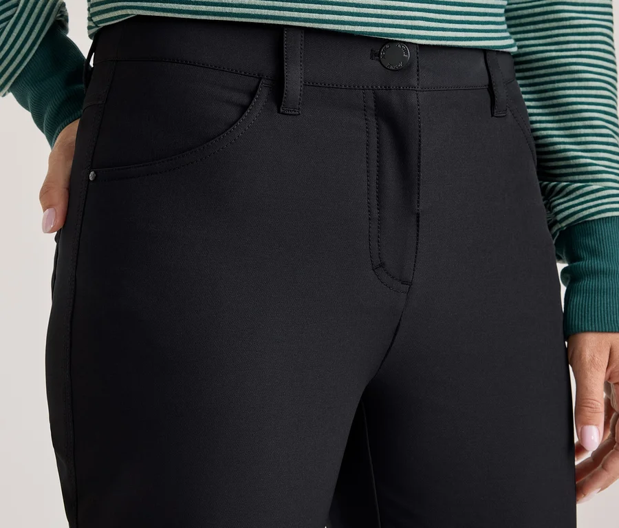 Nahaufnahme einer Person in schwarzer Hose und grün-weiß gestreiftem Langarmshirt, mit einer Hand an der Hüfte.