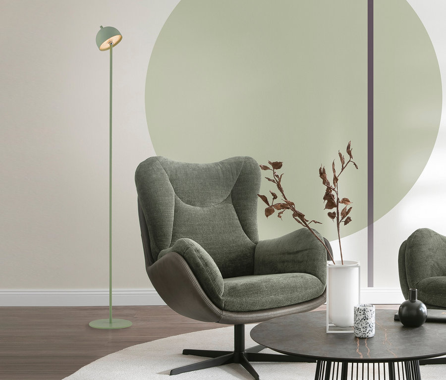 Grüner Sessel, hellgrüne SCHÖNER WOHNEN-Kollektion Akku-Stehleuchte »Bellis« und runder Couchtisch mit Deko auf weißem Teppich in einem Wohnzimmer mit hellgrünem Wandkreis.