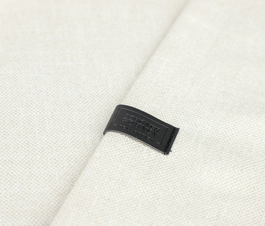 Nahaufnahme eines off-white SCHÖNER WOHNEN-Kollektion Ösenvorhangs »COAST« mit einem schwarzen Etikett, auf dem 'SCHÖNER WOHNEN KOLLEKTION' geprägt ist.