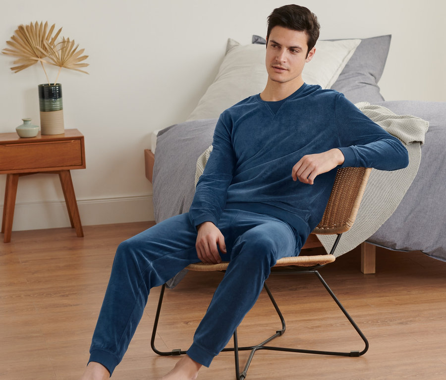 Mann sitzt in dunkelblauem Nicki-Pyjama auf einem Stuhl.