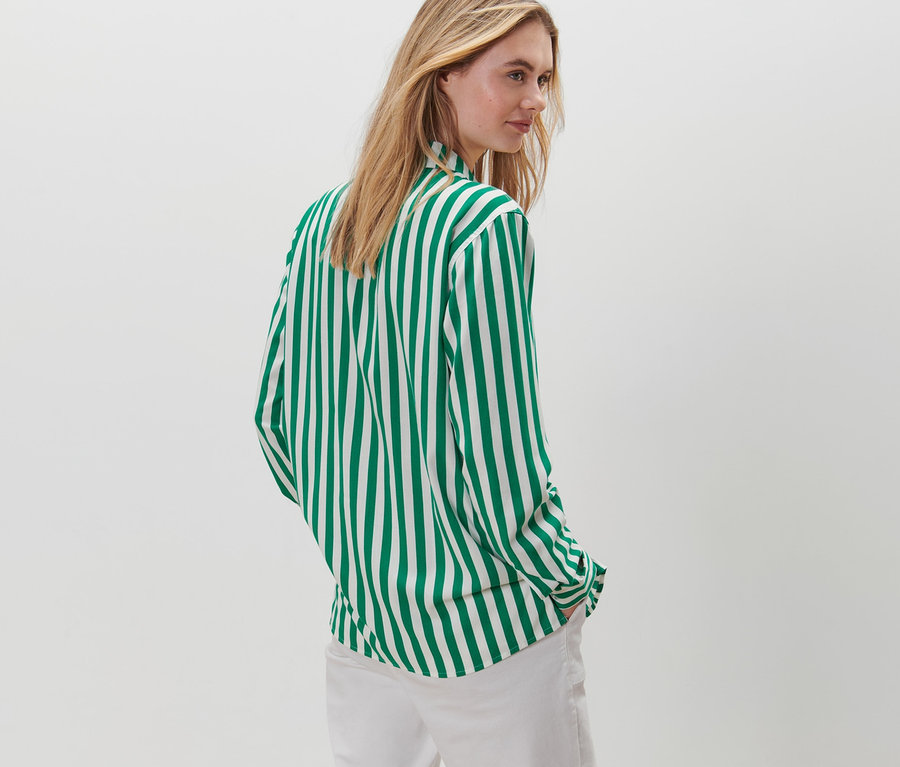 Frau posiert in gestreifter Bluse, grün und weiß, und weißen Hosen.