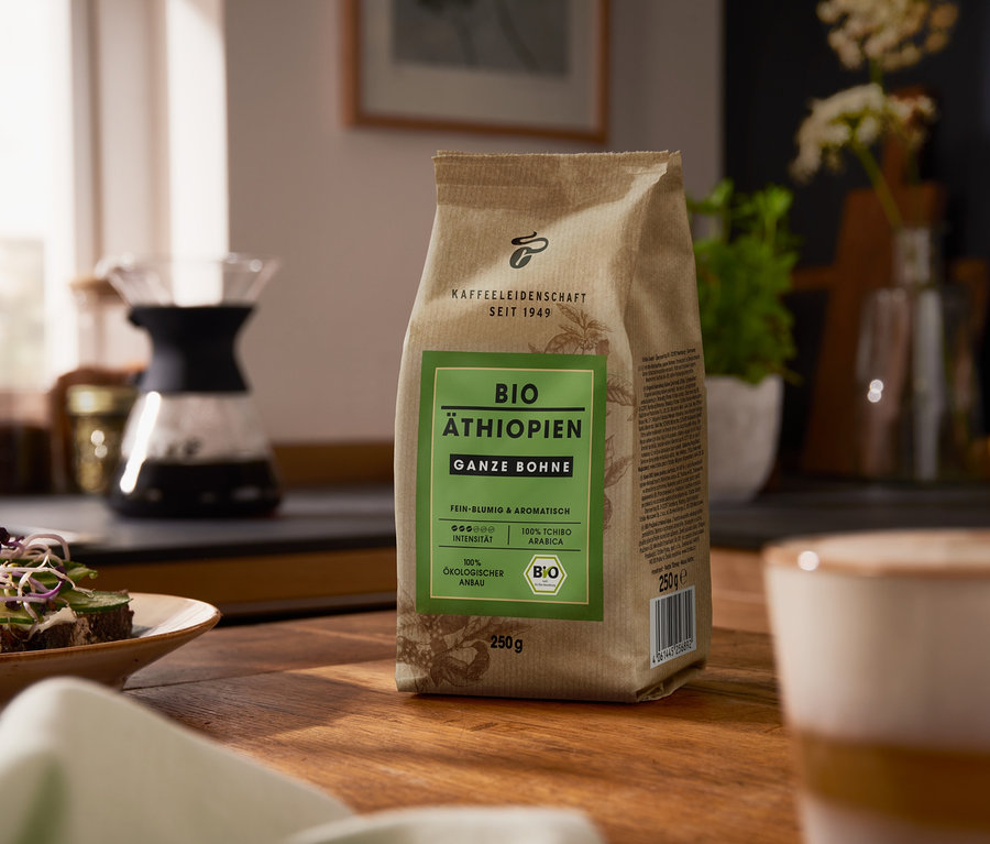 Auf einem Holztisch steht eine Packung Bio Äthiopien - 250 g Ganze Bohne. Im Hintergrund befindet sich eine Kaffeemaschine.