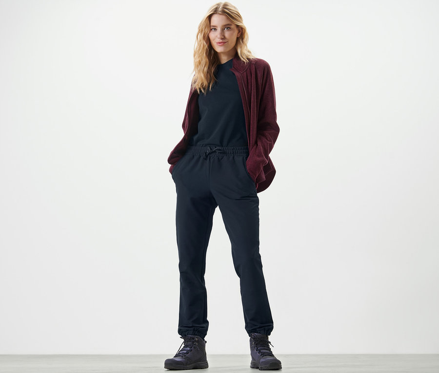 Blonde Frau steht mit Händen in den Taschen der Softshell-Joggpants.