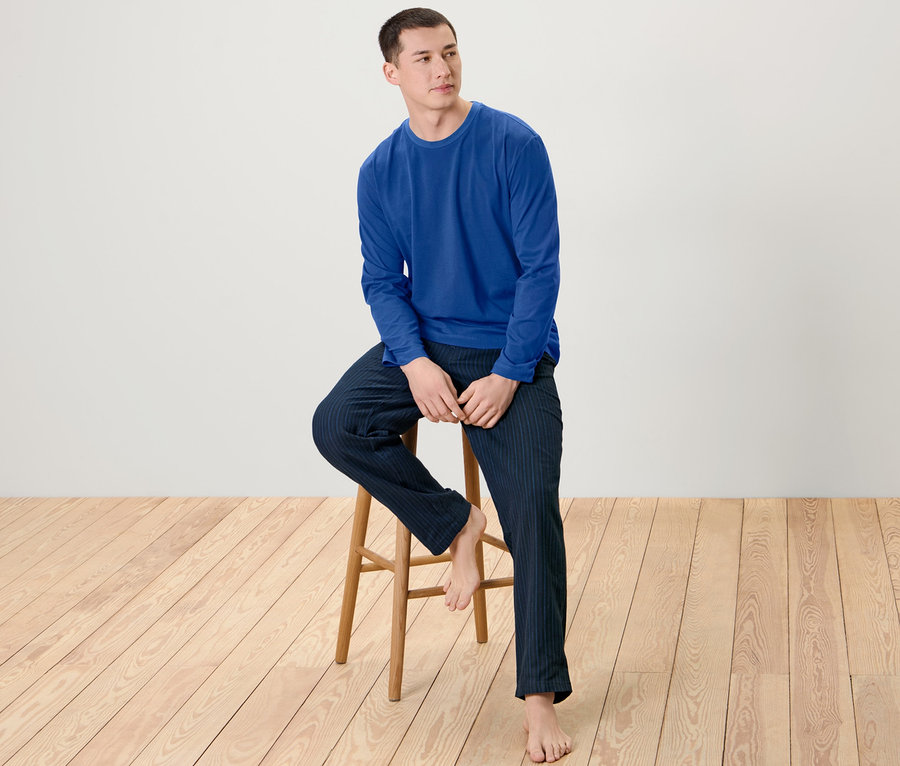 Mann sitzt auf einem Holzhocker und trägt einen Herren-Pyjama mit Flanellhose.