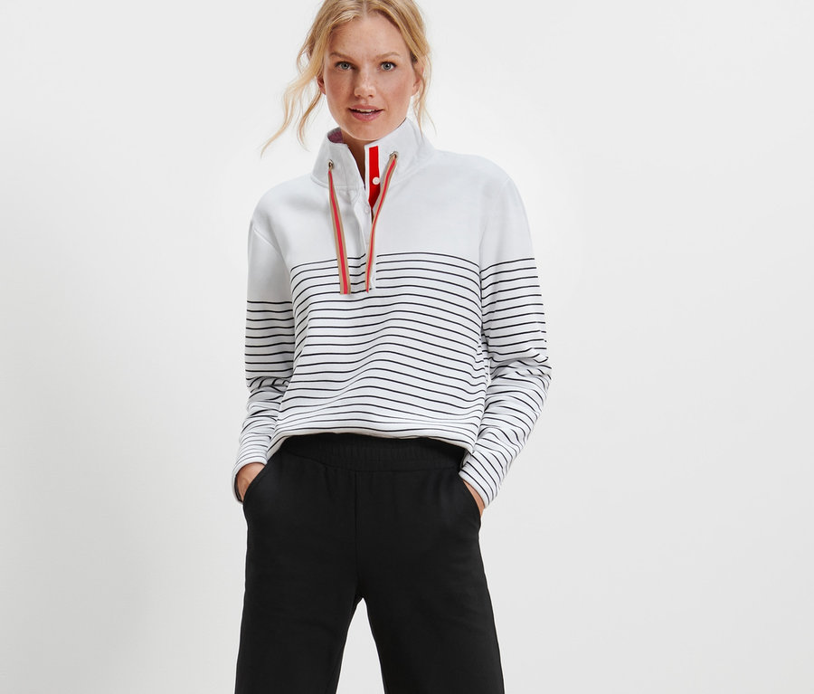 Frau posiert in einem gestreiften Sweatshirt und einer schwarzen Hose.
