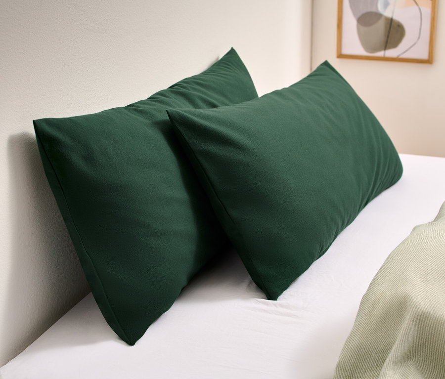 Zwei grüne Biber-Kopfkissenbezüge liegen auf einem weißen Bett.