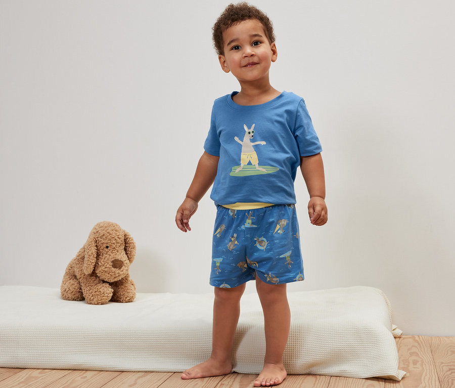 Ein Junge steht auf einer Matratze und trägt einen blauen Kinder-Shorty-Pyjama mit Känguru.
