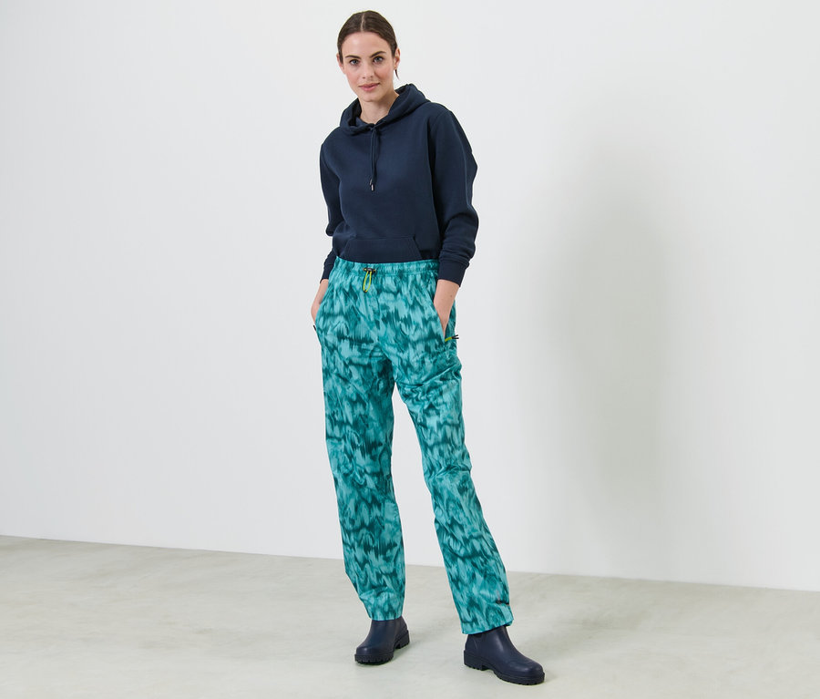 Frau steht mit Händen in den Taschen einer Regenhose mit Alloverprint.