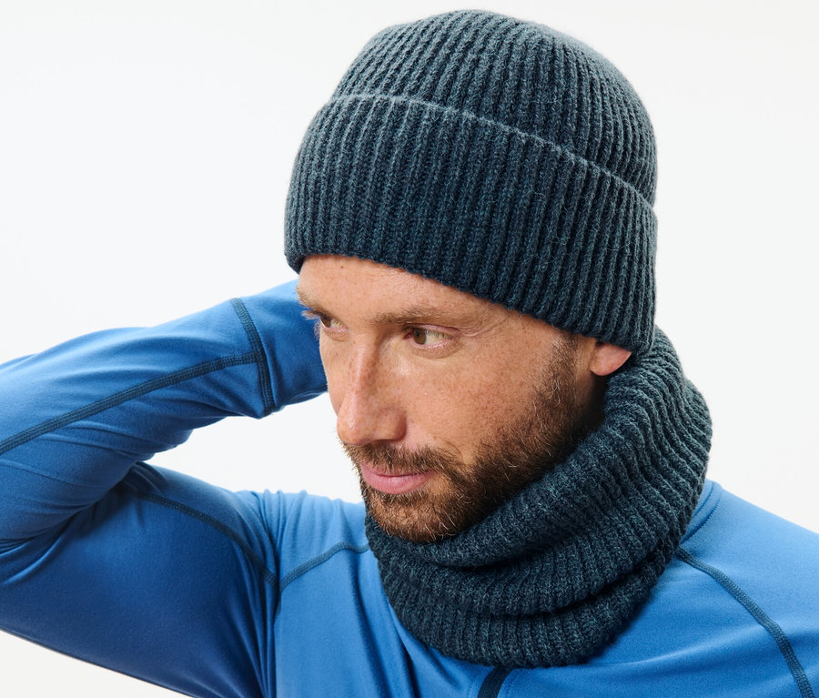 Ein Mann mit blauem Pullover und Strickschlauchschal richtet seine Mütze.