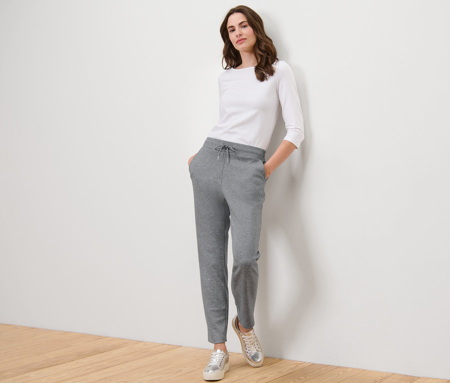 Frau posiert in grauer Joggpants und weißem Oberteil.