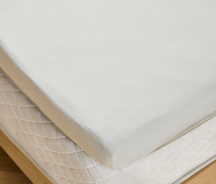 Detailansicht eines offwhite Topper-Spannbettlakens Normalgröße auf einer Matratze auf einem Holzrahmen.