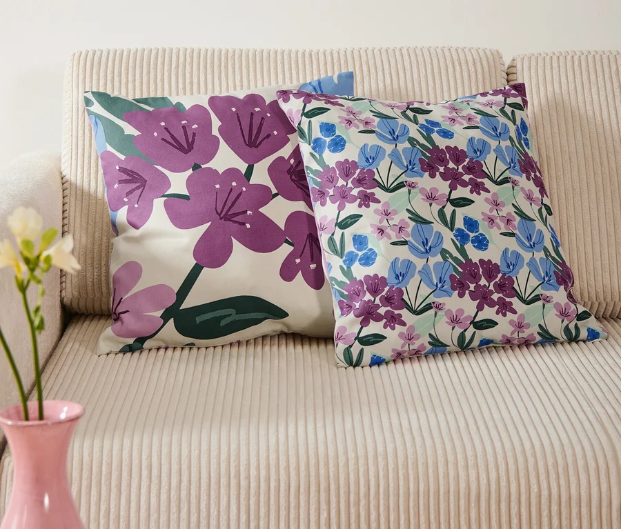 Zwei Dekokissenbezüge mit Blumenmuster liegen auf einem beigen Sofa, darüber hängt ein blaues Bild mit Blumen in einer Vase.