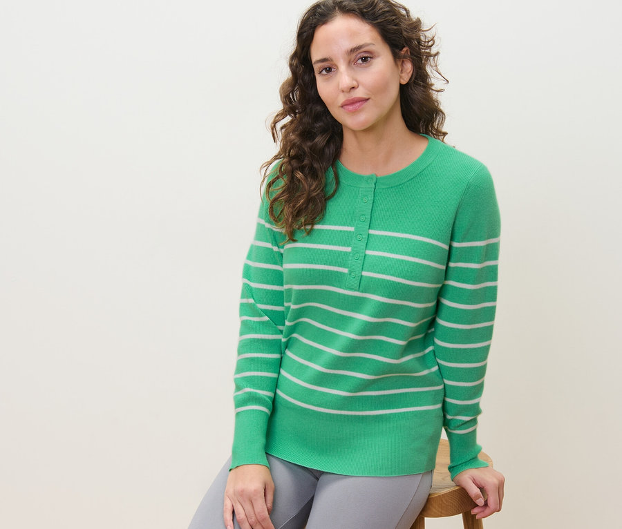Eine Frau sitzt auf einem Hocker und trägt einen gestreiften Feinstrickpullover.