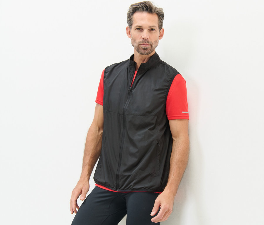 Mann an eine Wand gelehnt, trägt eine Funktionsweste.