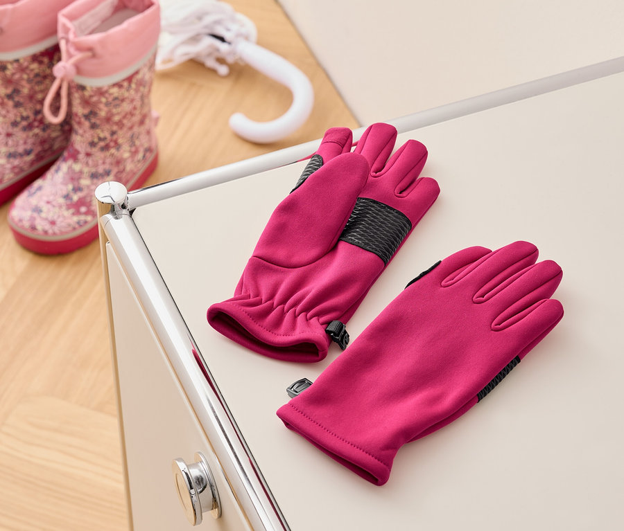 Ein Paar pinke Handschuhe liegen auf einem cremefarbenen Tisch neben rosa Kindergummistiefeln und einem weißen Regenschirm.