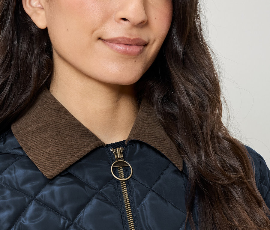 Detailaufnahme einer Damensteppjacke mit braunem Cordkragen und goldenem Reißverschluss.