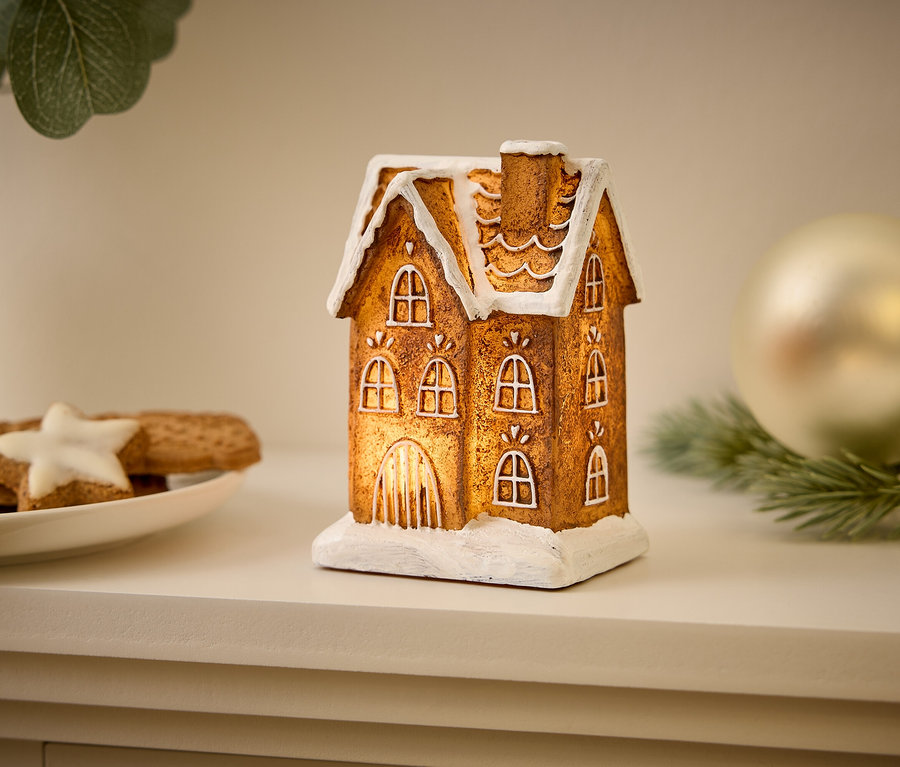 Ein dekoratives Lichthaus steht auf einem Regal neben Weihnachtsplätzchen und einer Kugel.