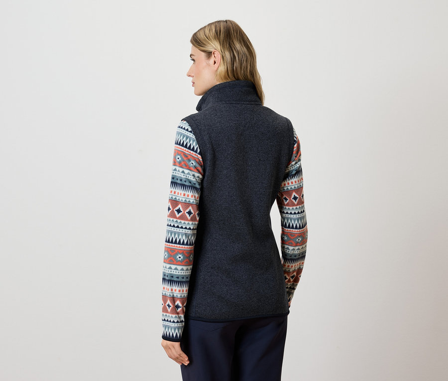 Frau mit dem Rücken zur Kamera trägt eine dunkelgraue Fleeceweste und eine blaue Hose.