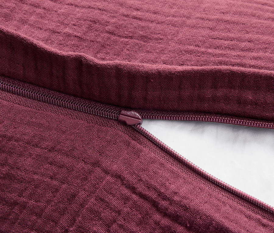 Detailaufnahme einer bordeauxfarbenen Stoffstruktur mit geöffnetem Reißverschluss.