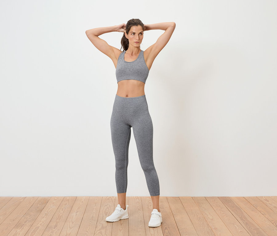 Frau posiert in grauem Sport-BH und Leggings.