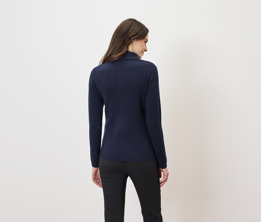 Rückansicht einer Frau mit langen braunen Haaren, die einen dunkelblauen Rollkragenpullover und eine schwarze Hose trägt.