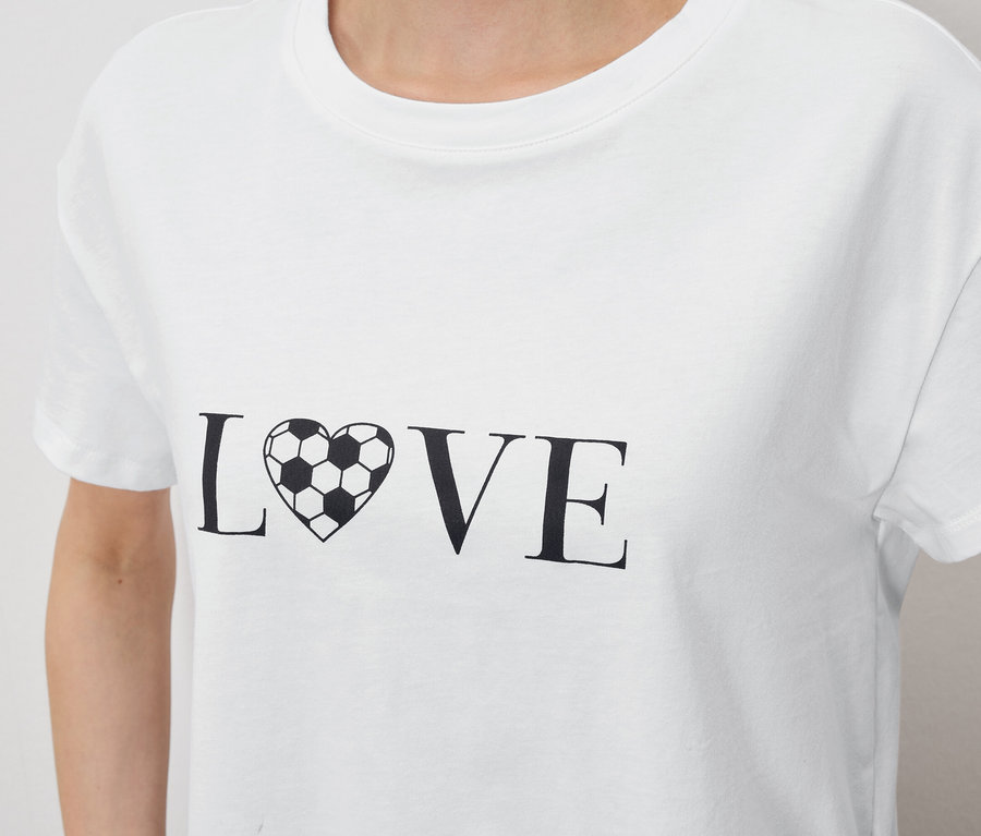 Nahaufnahme einer Person, die ein weißes T-Shirt mit dem Aufdruck "LOVE" trägt, wobei das "O" durch ein fußballförmiges Herz ersetzt wurde.