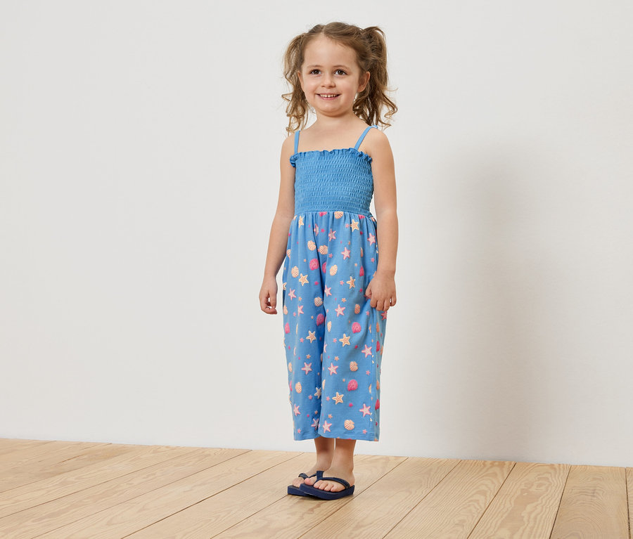 Ein Mädchen mit Zöpfen trägt einen blauen Jumpsuit mit Sternen und Muscheln.