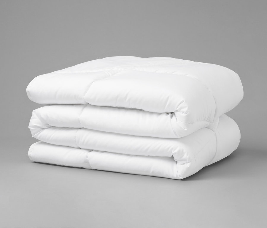 Gefaltete, weiße Steppdecke liegt auf grauem Untergrund.