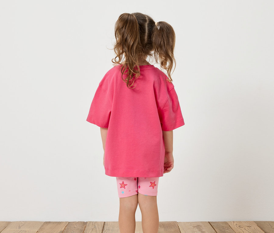 Mädchen von hinten, trägt ein pinkes T-Shirt und Leggings mit Sternenmuster.