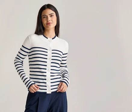Frau mit dunkelbraunen Haaren trägt eine weiß-blau gestreifte Strickjacke mit Knöpfen und eine marineblaue Hose.