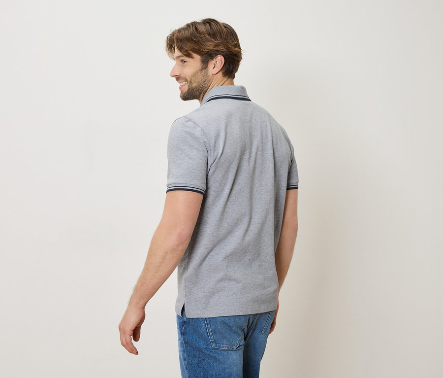 Mann von hinten in einem grauen Poloshirt und Jeans, lächelnd.