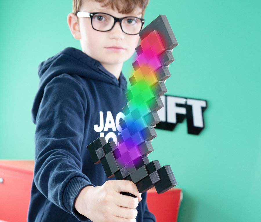 Junge mit Brille hält ein Minecraft-Schwert in der Hand, das in Regenbogenfarben leuchtet.