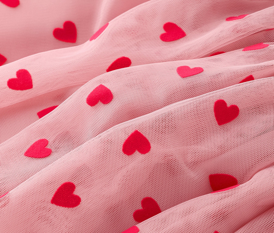 Nahaufnahme von gerafftem, rosa Tüllstoff mit roten Herzchen.